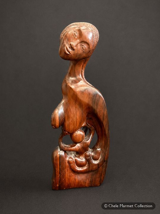 Slender carved reddish-brown wooden figure of a mother holding a nursing baby.
