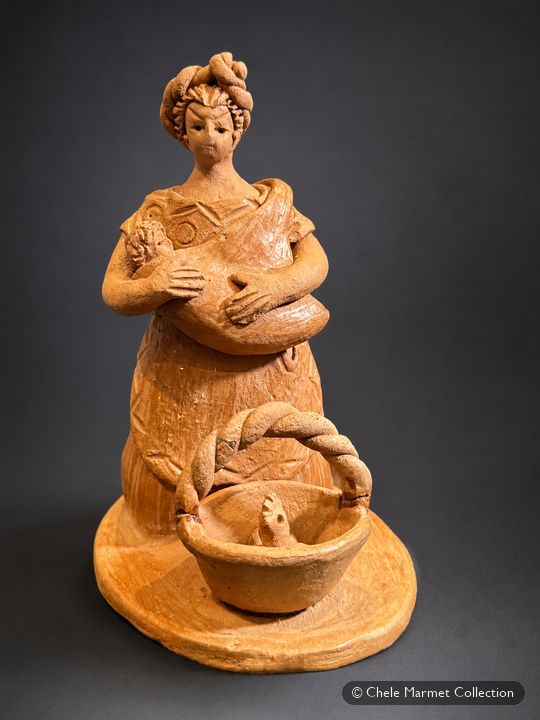 Terracotta figure of a woman in a long dress with a baby in a sling at her chest and a basket holding a chicken in front of her.
