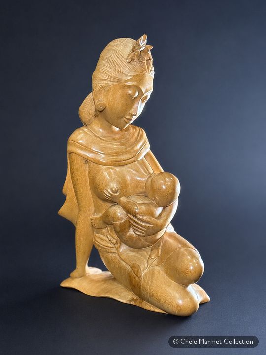 Pale carved wooden figure of a kneeling woman nursing a baby.