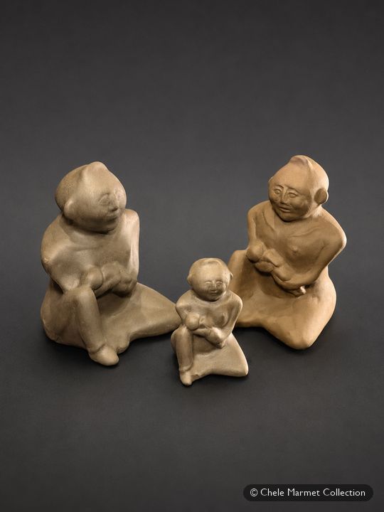 Three small grey clay figures: two seated adults and a small child between them.