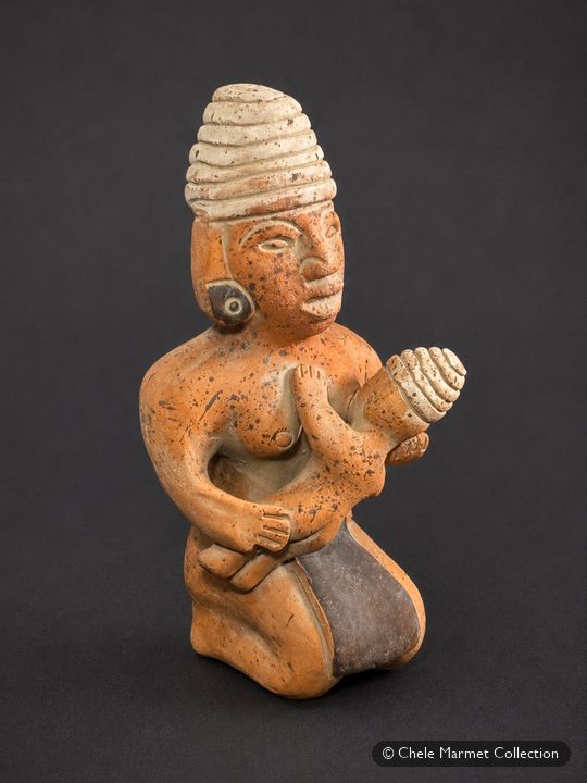 Terracotta kneeling figure of a woman with large ear discs and a tall headdress, nursing a baby.