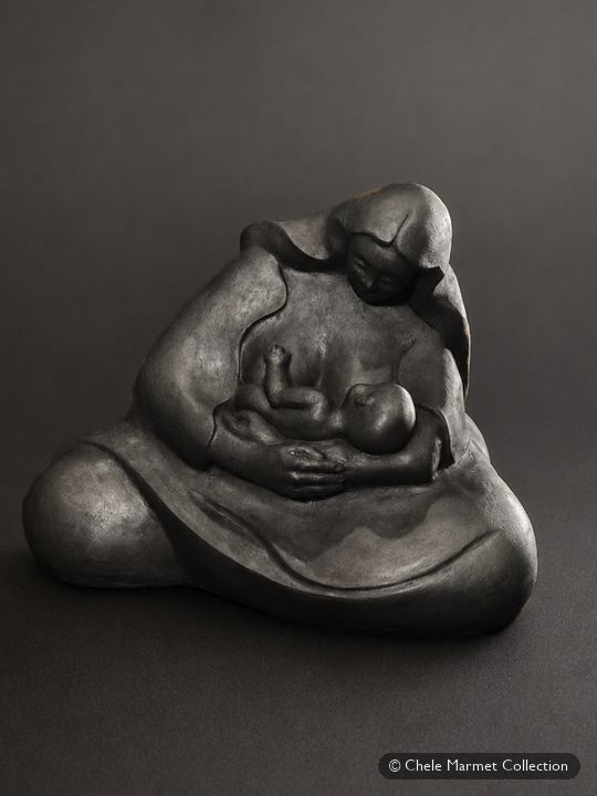 Smooth, dark sculpture of a seated, shawl-wrapped mother bent over a nursing baby.