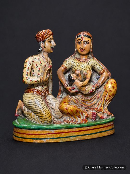 Painted figurine of a seated couple on a green base; the woman nurses a baby.