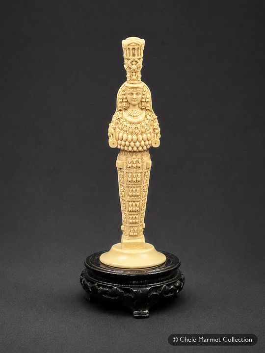 Tall ivory-coloured statuette of the many-breasted Artemis of Ephesus on a black stand.