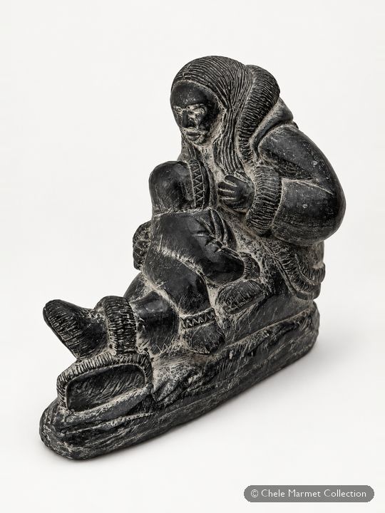 Dark grey polished carving of a mother in a hooded parka holding a baby.