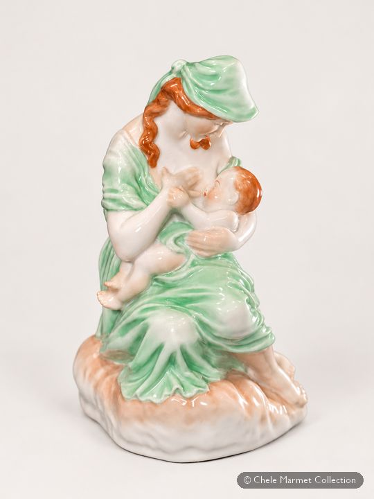 Porcelain figure of a red-haired woman in a green dress and headscarf, seated and nursing a baby.