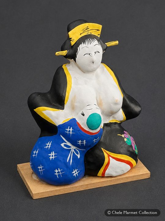 Painted papier-mâché figure of a woman with a black topknot and white face holding a child wrapped in blue cloth.