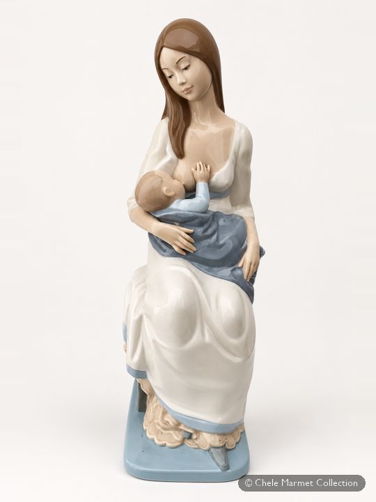 Porcelain figure of a long-haired woman in a white and blue dress, seated and nursing a baby.