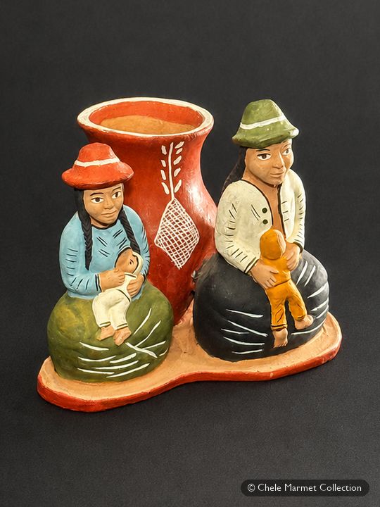 Small brightly painted ceramic scene of two seated figures in hats beside a pot.