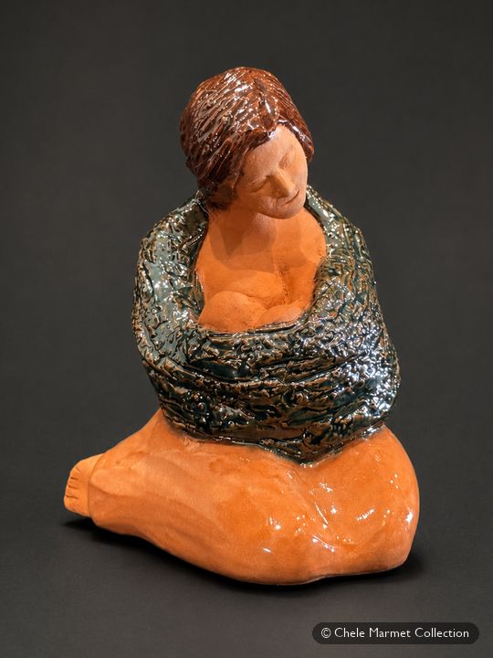 Ceramic seated mother with dark hair and an orange skirt, wrapped in a dark blanket with her baby.