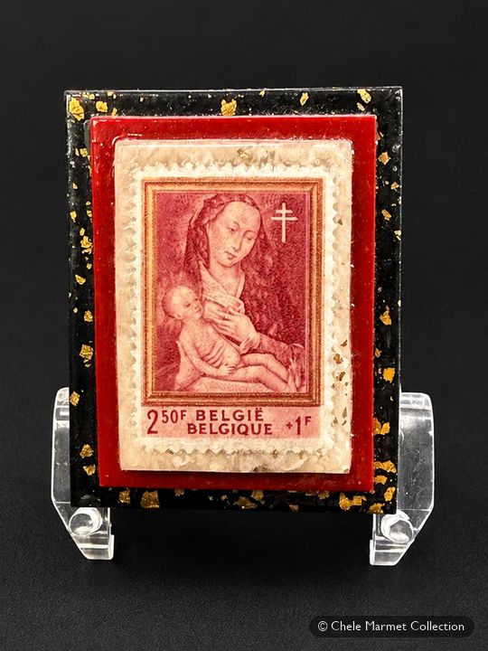 Red stamp of a Madonna and child, mounted on a small red and gold card on a clear stand.
