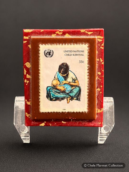 United Nations stamp of a mother nursing a baby, mounted on a red card.